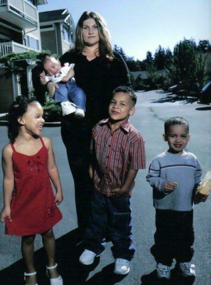 Woman holding baby with three smiling children outside in a neighborhood, inspiring facts about family and happiness.
