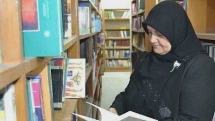 Woman in a black hijab browsing books in a library aisle, discovering inspiring facts better than watching the news