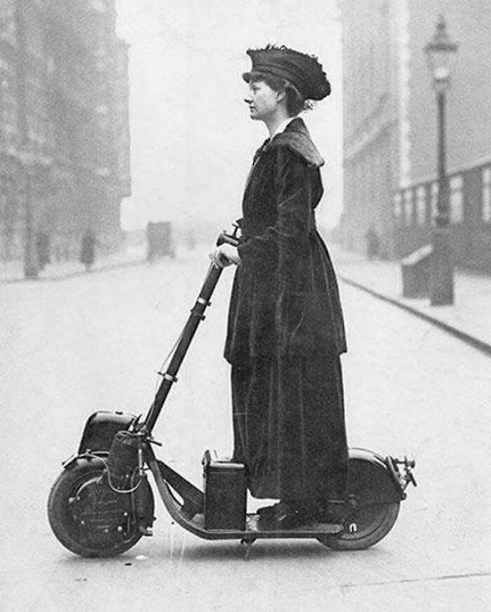 Woman in vintage attire standing on an early electric scooter on a deserted city street with inspiring facts theme.