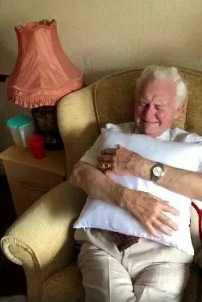 Elderly man smiling warmly while hugging a pillow, illustrating inspiring facts about joy and comfort at home.