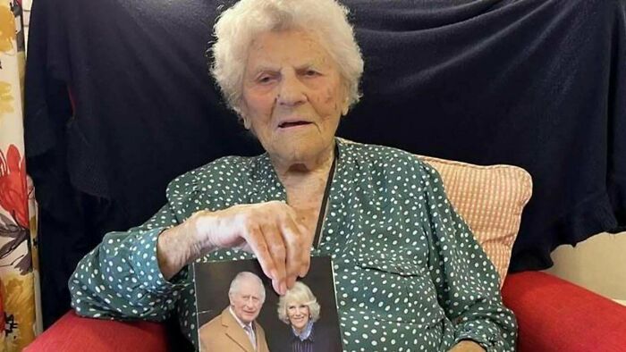 Elderly woman sitting on a red chair holding a photo of an older couple, inspiring facts concept better than news.