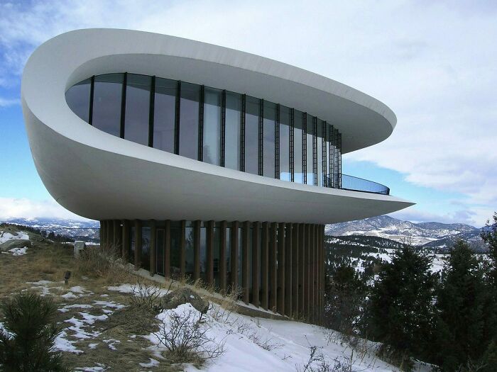 Modern curved TV house with large glass windows overlooking snowy mountainous landscape, iconic TV houses real life design.
