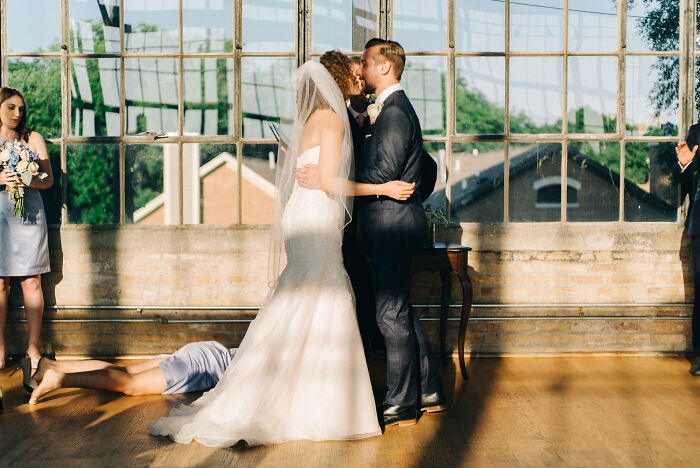 Bride and groom embracing indoors while a person lies on the floor, capturing the moment before disaster struck rope broke.