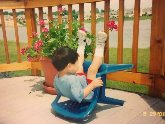 Child falling backward in a blue plastic chair moments before a backyard accident captured perfectly.