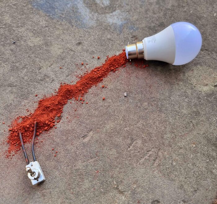 Light bulb connected to loose wires with red powder spilled between, illustrating people handling electronics the wrong way.
