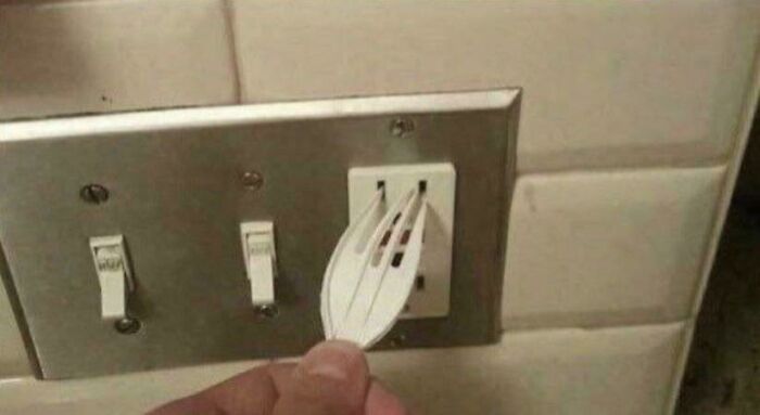 Hand holding a plastic fork inserted into an electrical outlet illustrating improper electronics handling.