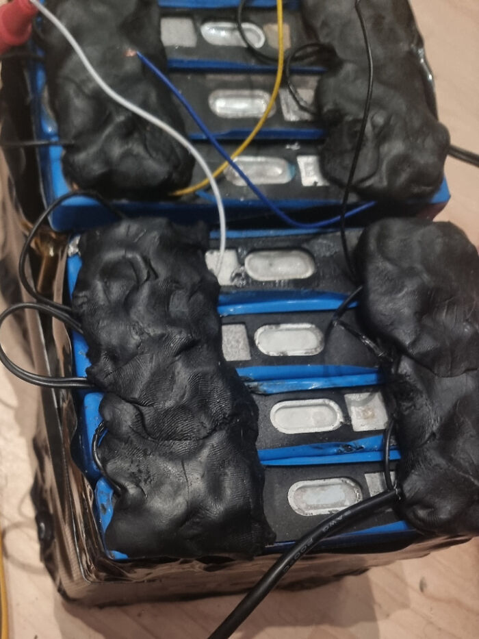 Close-up of poorly soldered and mishandled electronics battery pack with numerous wires and black sealant visible.