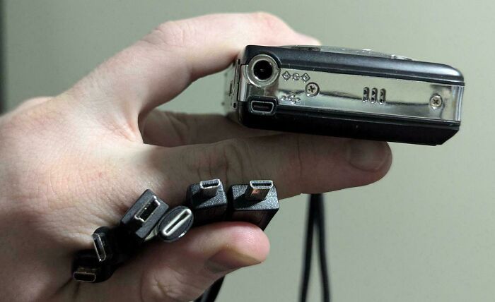 Hand holding multiple electronic charging cables near a device port, illustrating common mistakes handling electronics.