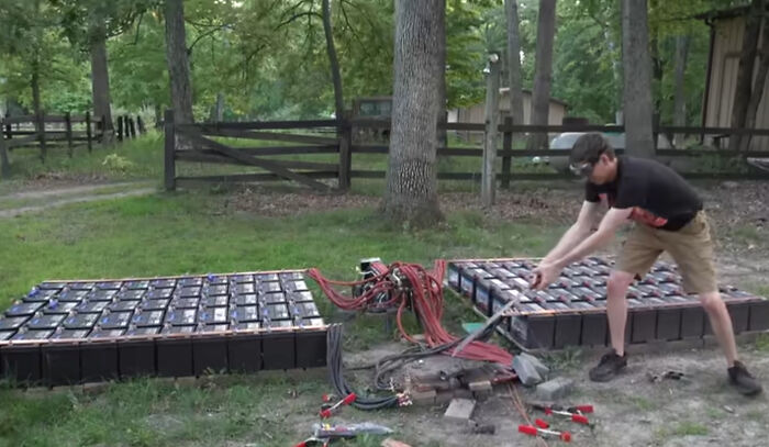 Man working on large battery packs outdoors surrounded by cables and tools, illustrating electronics handled the wrong way.