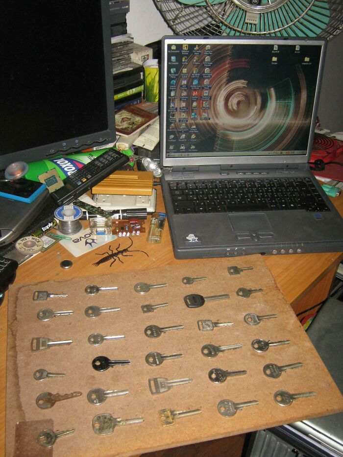 Cluttered workspace with an open laptop, electronic parts, soldering materials, and keys scattered on a wooden board.