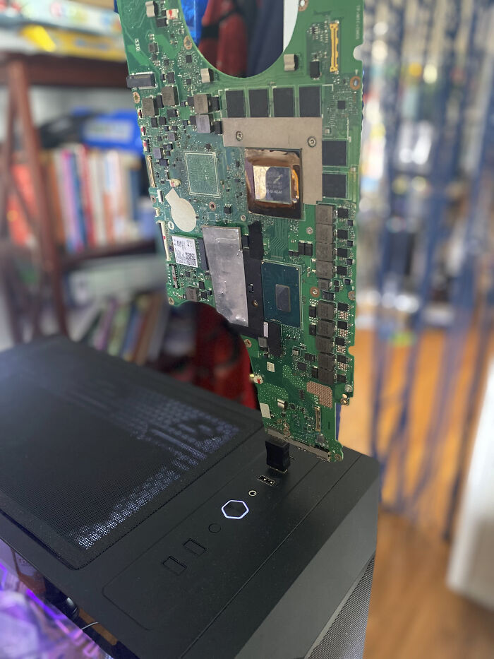 Exposed computer motherboard precariously connected to a desktop case, highlighting improper electronics handling and soldering risks.