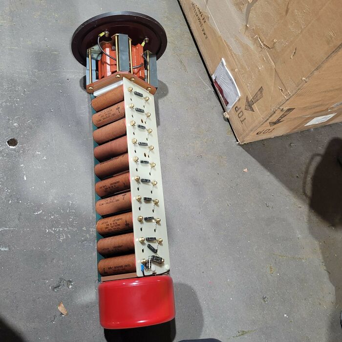 Vintage electronic component with large capacitors and resistors laid on a concrete floor, showcasing electronics handling errors.