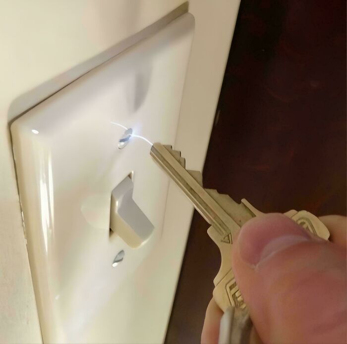 Person using a metal key to tamper with an electrical switch, showing unsafe handling of electronics and potential hazards.