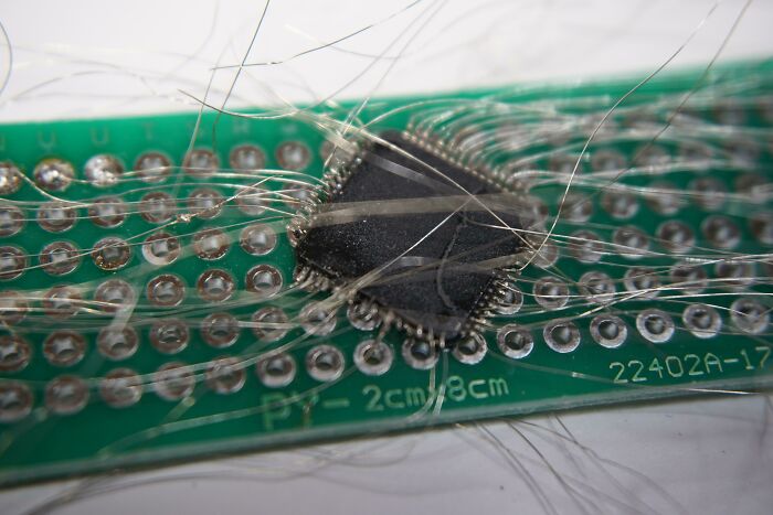 Close-up of damaged electronic chip with many broken wires, showing incorrect handling and soldering attempts on a circuit board.