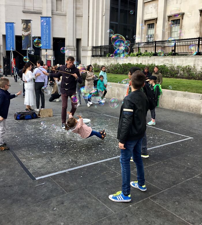 Child slipping on wet ground surrounded by bubbles as people watch, capturing the split second before disaster.