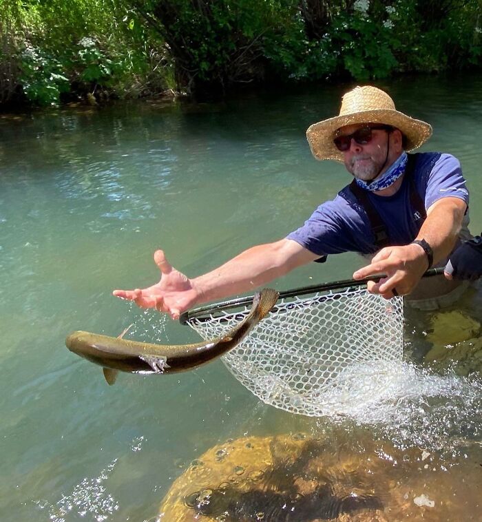 Man struggling to catch a fish mid-air with a net in a river, capturing a split second before disaster hits hilariously.