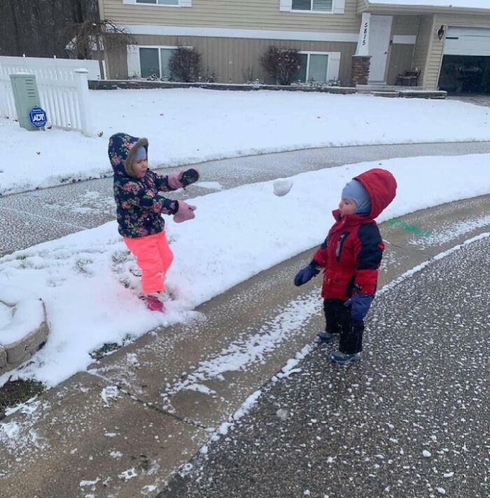 Two toddlers in winter clothes about to have a snowball fight capturing the split second before disaster.