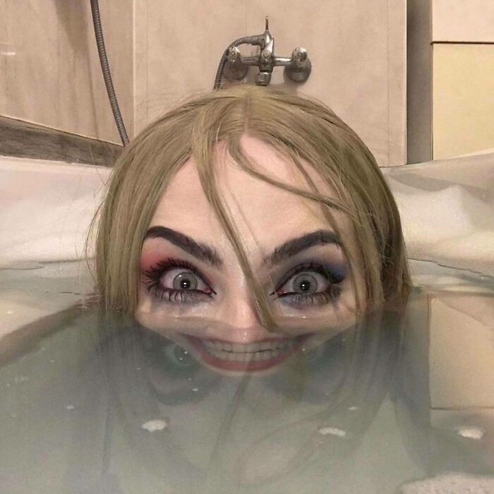 Woman with colorful eye makeup and distorted smile partially submerged in water in a weird and cursed picture.