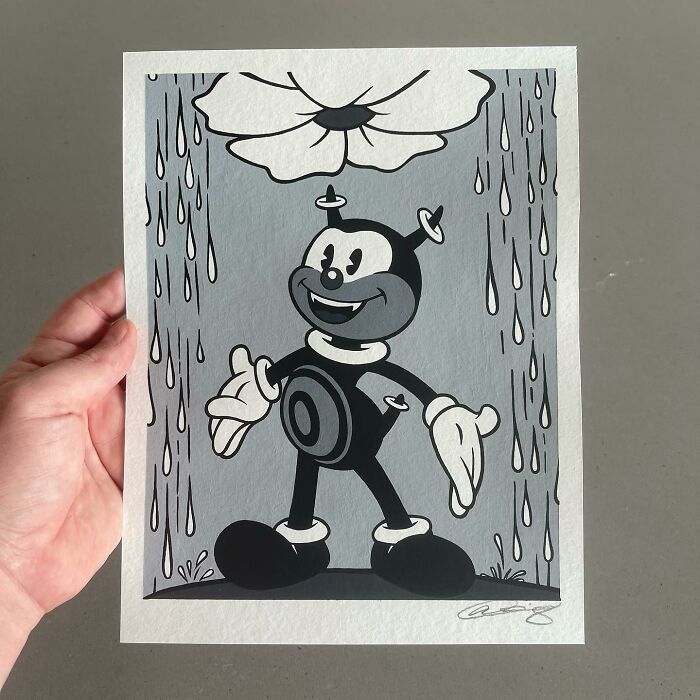 Hand holding pop culture and cartoon character mash-up artwork featuring a black and white vintage style figure under a flower.