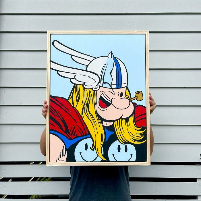 Person holding a framed pop culture and cartoon character mash-up artwork in bold colors against a gray wall.