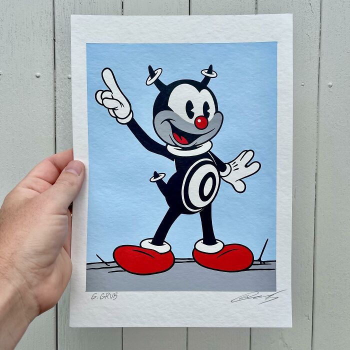 Hand holding pop culture and cartoon character mash-up artwork featuring a black and white figure with red shoes and nose.
