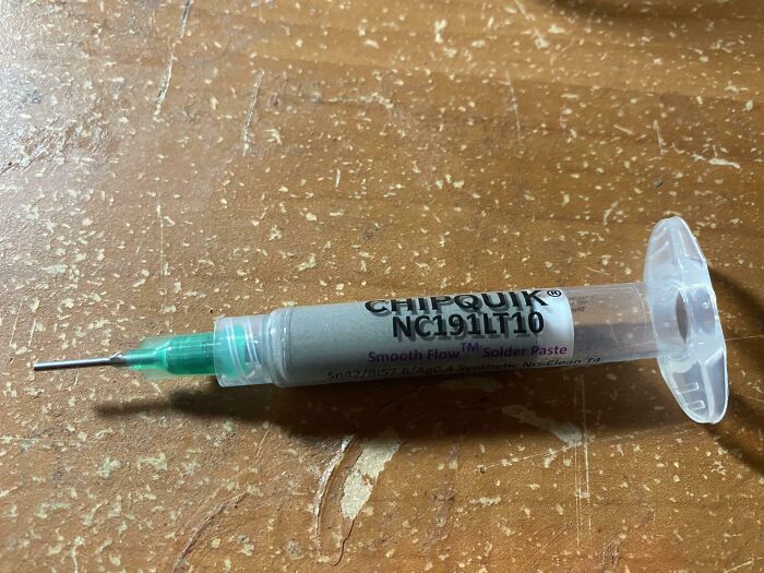 Solder paste tube on a worn wooden surface used for electronics soldering in DIY repair projects.