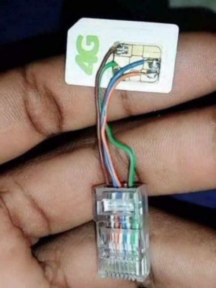 Hand holding a 4G SIM card with exposed wires soldered to an RJ45 connector, illustrating electronics handled the wrong way.