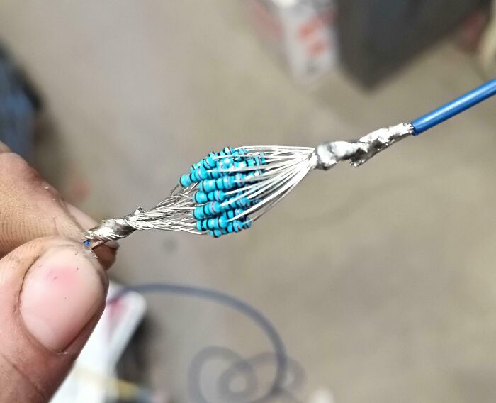 Close-up of a person holding a complex electronic wire bundle with resistors soldered poorly back together.