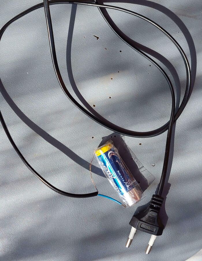 Improvised electronics repair showing a loose wire connected to a battery wrapped in plastic and an unplugged power cord.