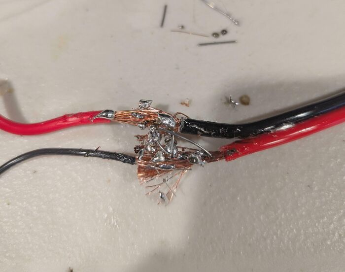 Messy and unsafe soldering on red and black wires with exposed copper and poor connections in electronics handling.