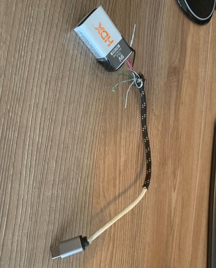 Exposed wires and a 9V battery connected to a USB-C cable, showing a risky electronics handling attempt without proper soldering.