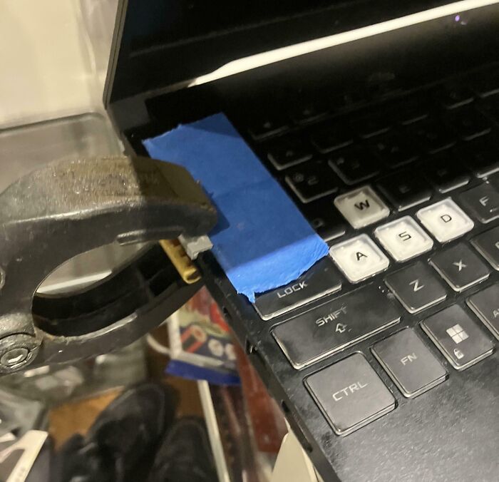Clamp attached to a laptop with tape holding a loose key cover, illustrating painful electronics handling mistakes.