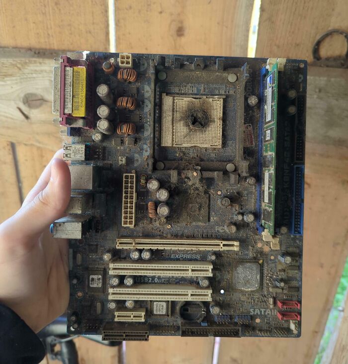 Burnt and dusty electronics motherboard held by hand, showing damage in a painful example of handling electronics wrong.