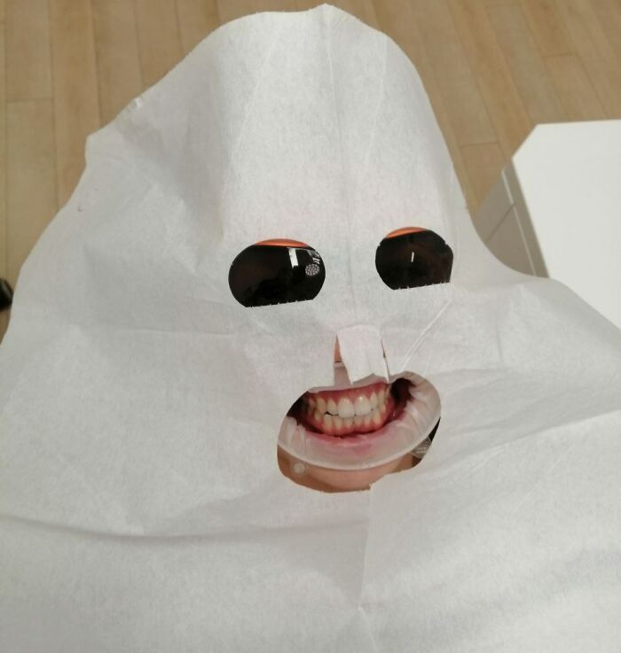 Weird and cursed pic of a person with sunglasses and a big smile under a white sheet with cut-out eyes and mouth.