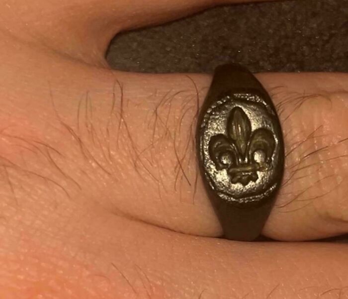 Close-up of a medieval history enthusiast's hand wearing a dark metal ring with a fleur-de-lis symbol.