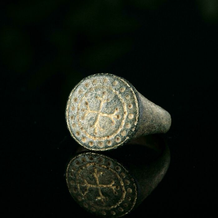 Medieval ring with cross design reflecting on black surface, representing medieval history enthusiasts' joy recently.