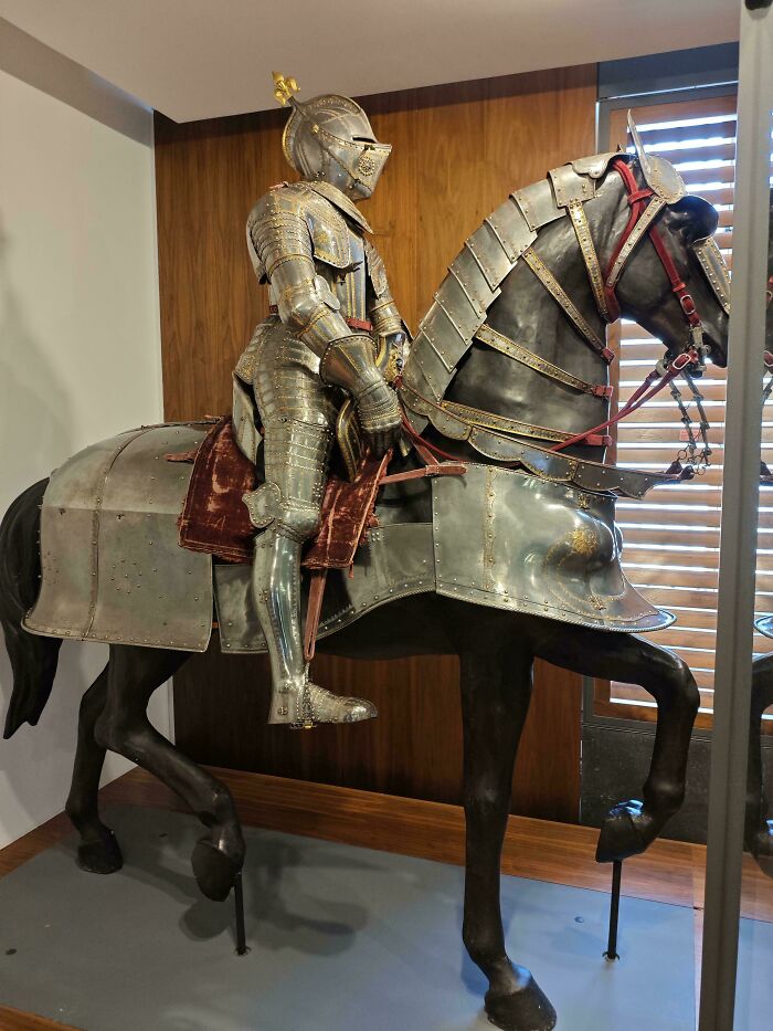 Medieval history enthusiasts exhibit a fully armored knight on a horse in a museum display with detailed medieval armor.