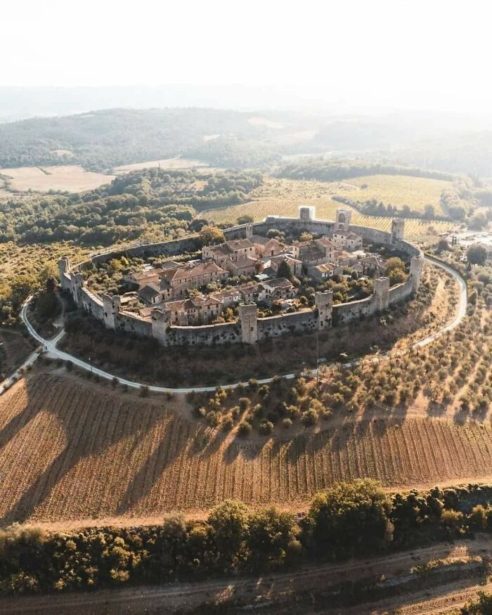 Aerial view of a medieval walled village surrounded by fields and forests, reflecting medieval history enthusiasm.