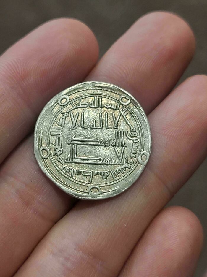 Close-up of a medieval coin with intricate Arabic inscriptions held between fingers for medieval history enthusiasts.