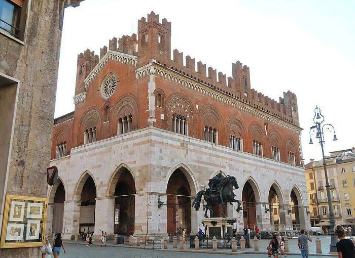 Medieval brick building with arched windows and statue, attracting medieval history enthusiasts in a lively public square.