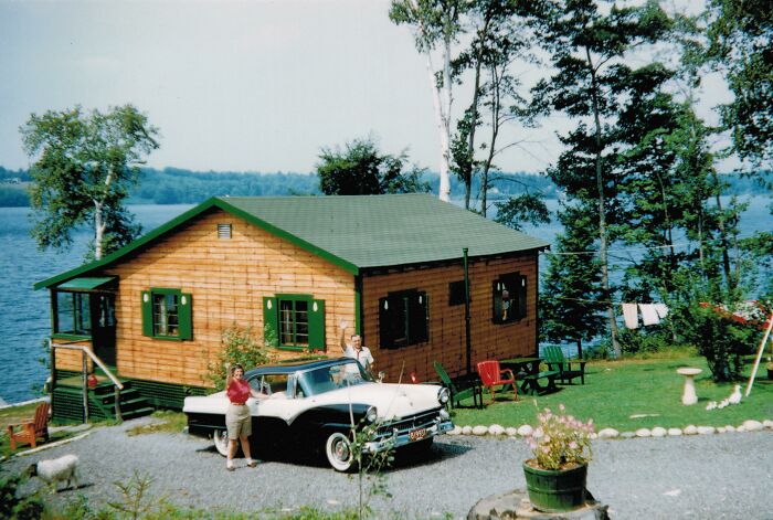Vintage vacation pic of a couple by a classic car outside a lakeside cabin, showing life before cell phones had cameras.
