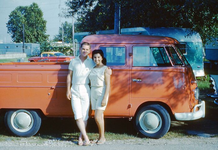 Couple posing beside a vintage orange Volkswagen pickup during a vacation, capturing a moment from before cell phone cameras existed.