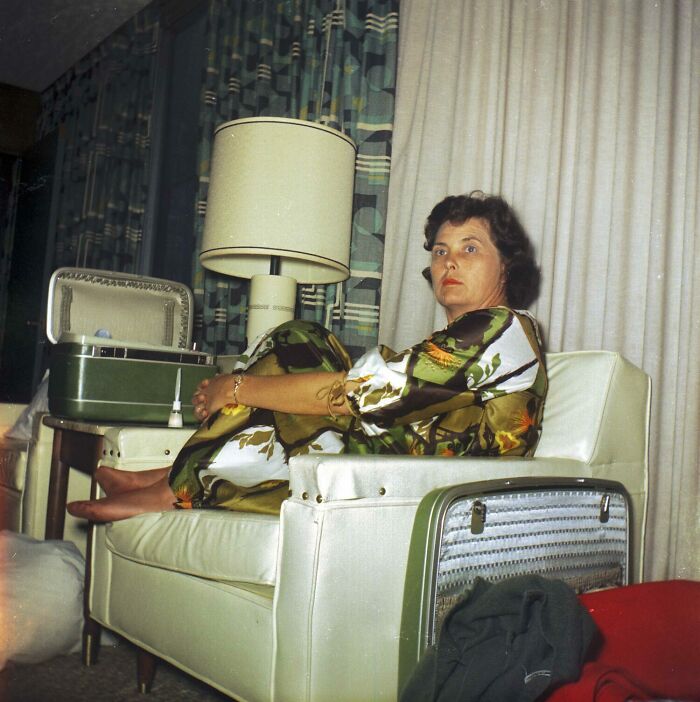 Woman relaxing on a vintage couch during vacation, surrounded by classic travel suitcases and a mid-century lamp.