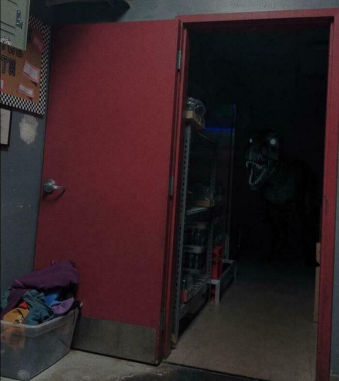 Dimly lit storage room with open red door revealing a dark figure resembling a dinosaur, highlighting unsettling job photos.