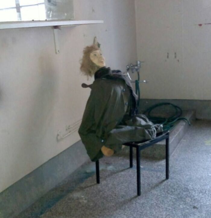 Creepy mannequin dressed in work clothes sitting on a chair in a dim, empty room in unsettling worker photo.