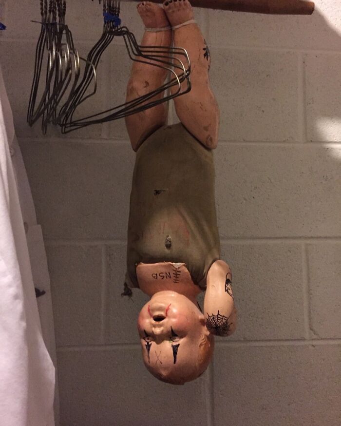 Creepy doll with tattoos and marks hanging upside down in a dimly lit room, unsettling worker photo.