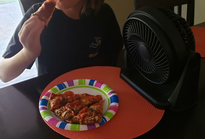 Child eating pizza near a new invention fan on a table, showcasing kids surprising parents with creative ideas.