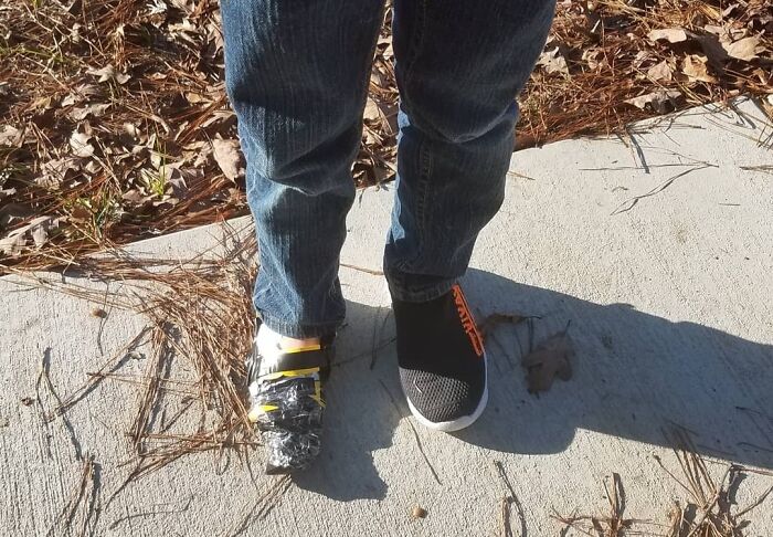 Child wearing one regular shoe and one homemade invention shoe made with duct tape and plastic on a concrete surface outdoors