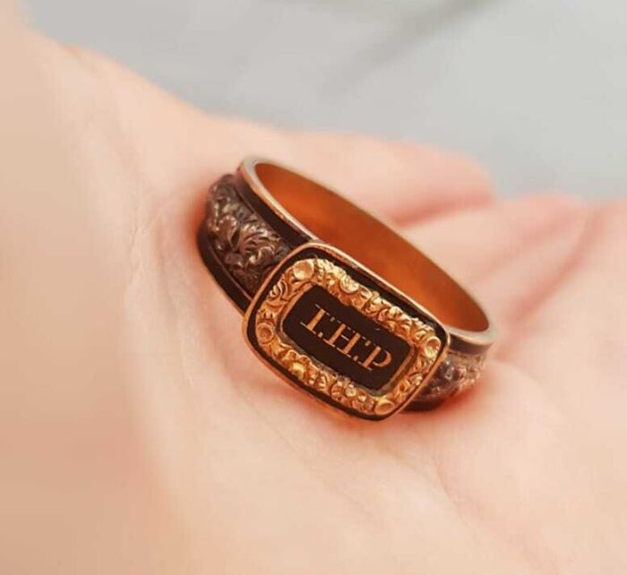 Antique ring with engraved initials held in palm, an old find with unknown origin and history.