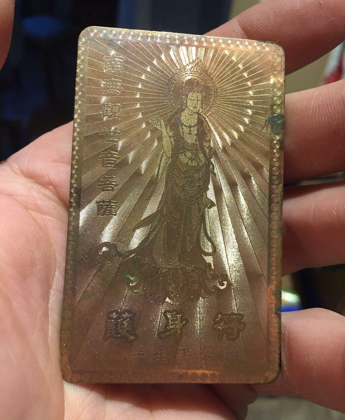 Person holding a vintage engraved metal plate with an old religious figure and ancient Asian characters found unexpectedly.